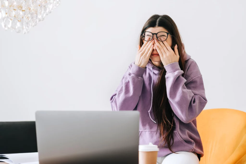 young woman rubs her eyes after using glasses front laptop eye pain fatigue concept